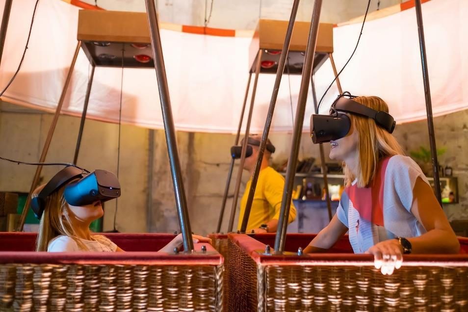 Drie mensen met VR-brillen staan in rieten ballonmanden van een VR-ballonvaartsimulator en lachen naar elkaar.
